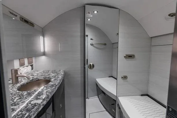 The modern lavatory of a private jet, featuring a granite-topped vanity with a bronze faucet and a toilet.