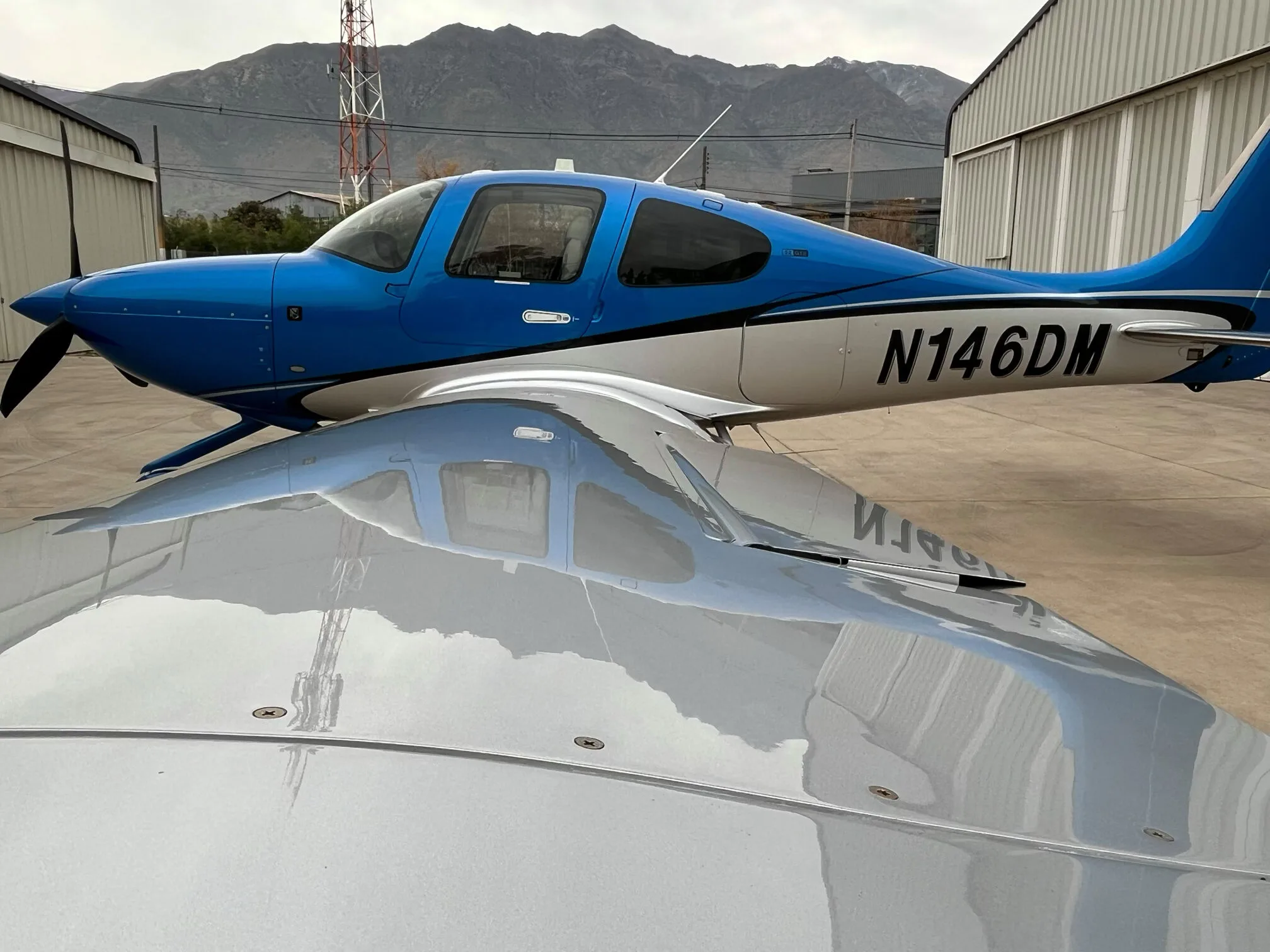 A side view of a blue and silver Cirrus SR22 GTS aircraft with N146DM registration, showing its reflection on the wing.