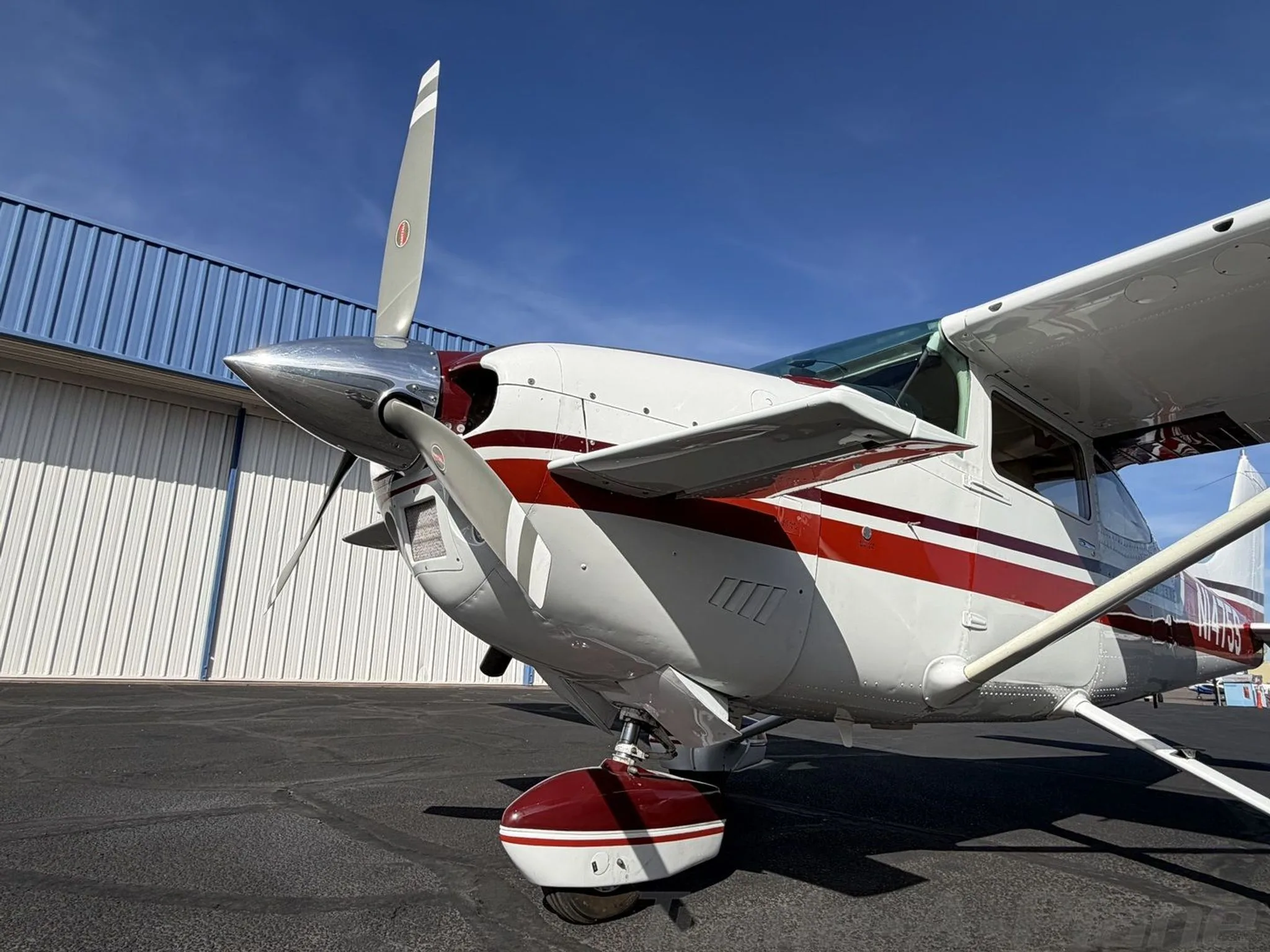 A low-angle front-left view of the propeller and landing gear of the white and red Cessna Skylane II.