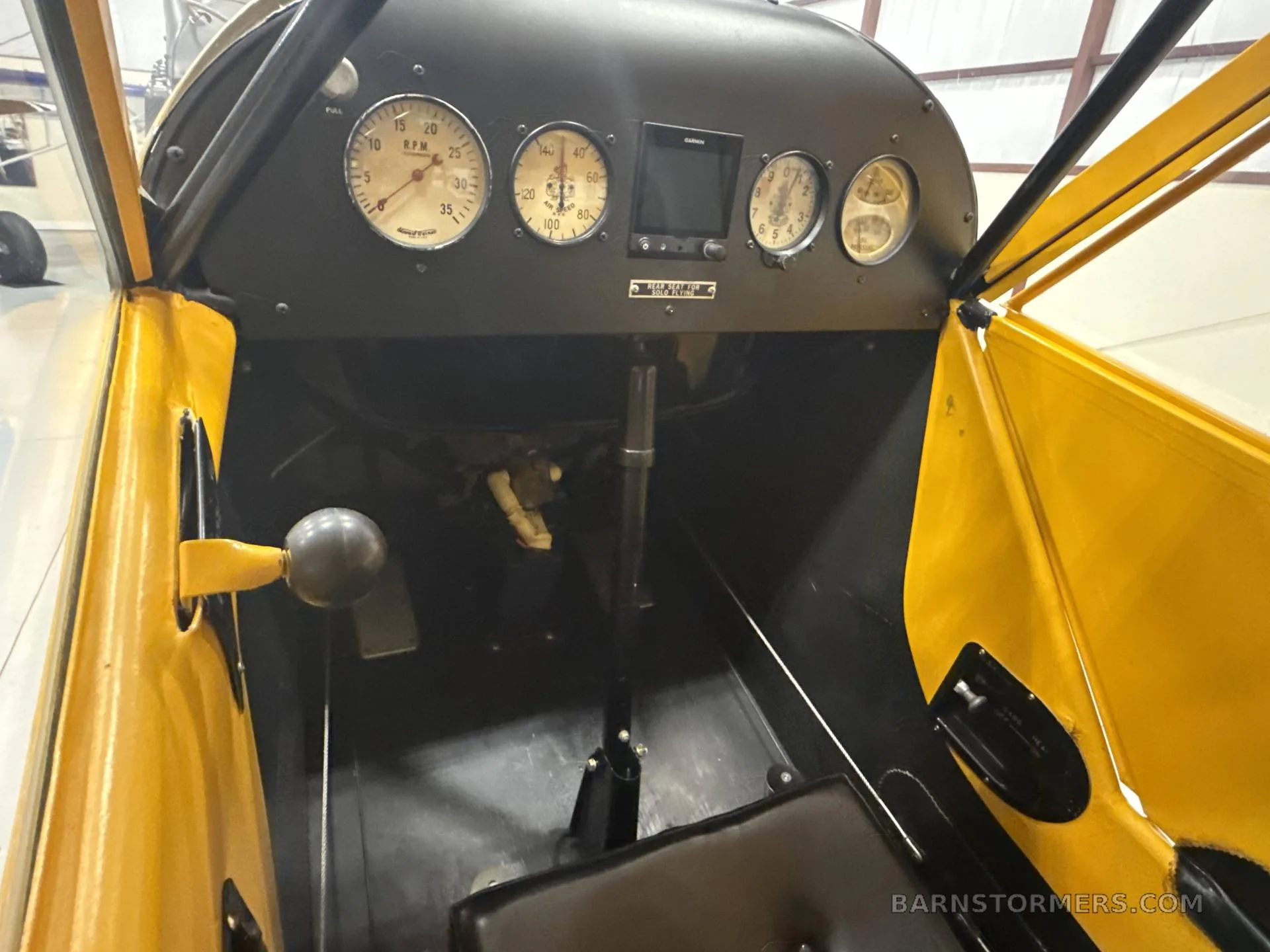 The simple instrument panel and controls of a yellow vintage aircraft cockpit.