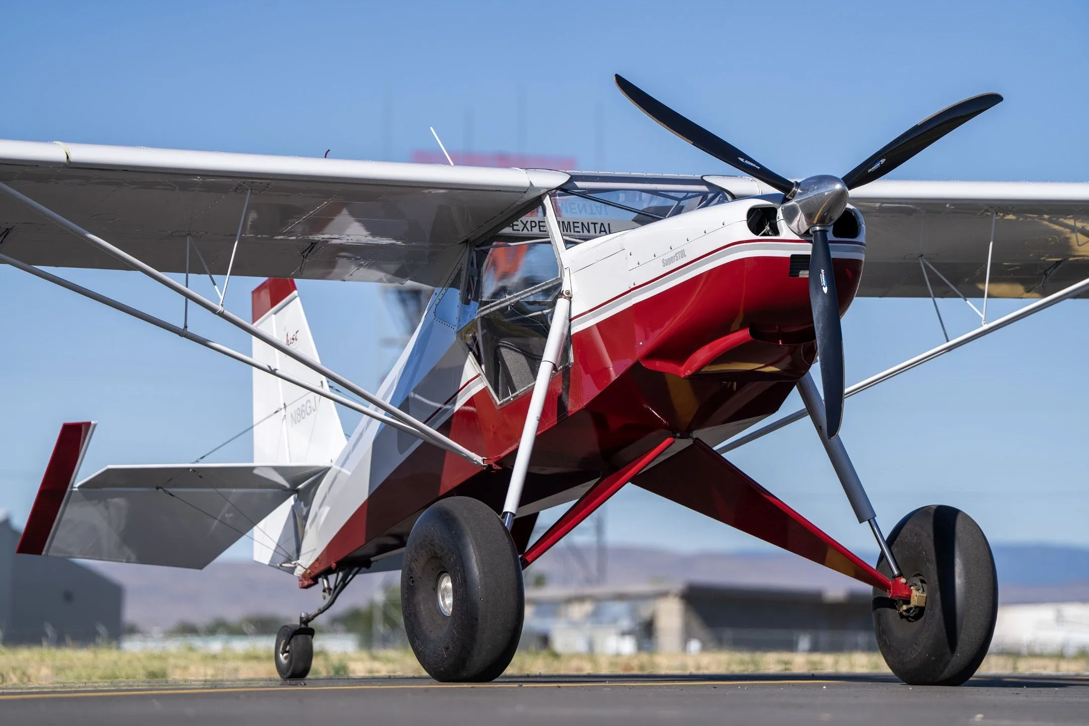 Front-right view of a red and white Just Aircraft SuperSTOL with large tundra tires on an airfield.