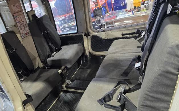 The grey fabric interior of a helicopter cabin, showing two rows of passenger seats with seatbelts.