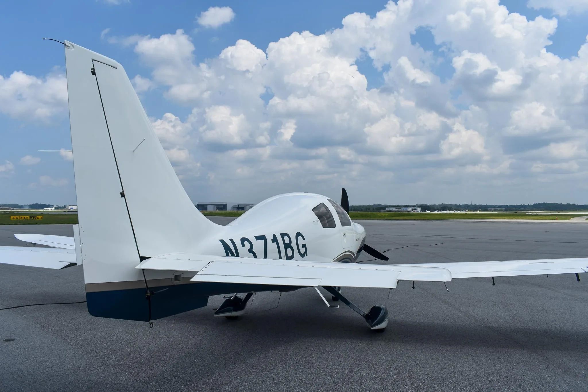 A rear view of the white and blue Columbia 400 aircraft, registration N371BG, parked on an airfield under a cloudy sky.