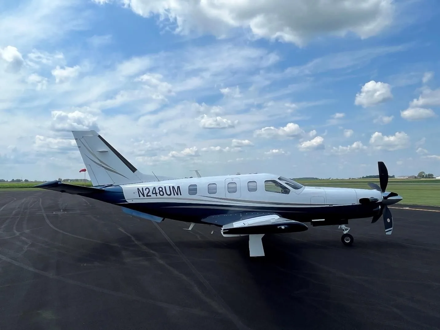 A side view of the N248UM aircraft, a white and blue turboprop, parked on an asphalt runway under a partly cloudy sky.