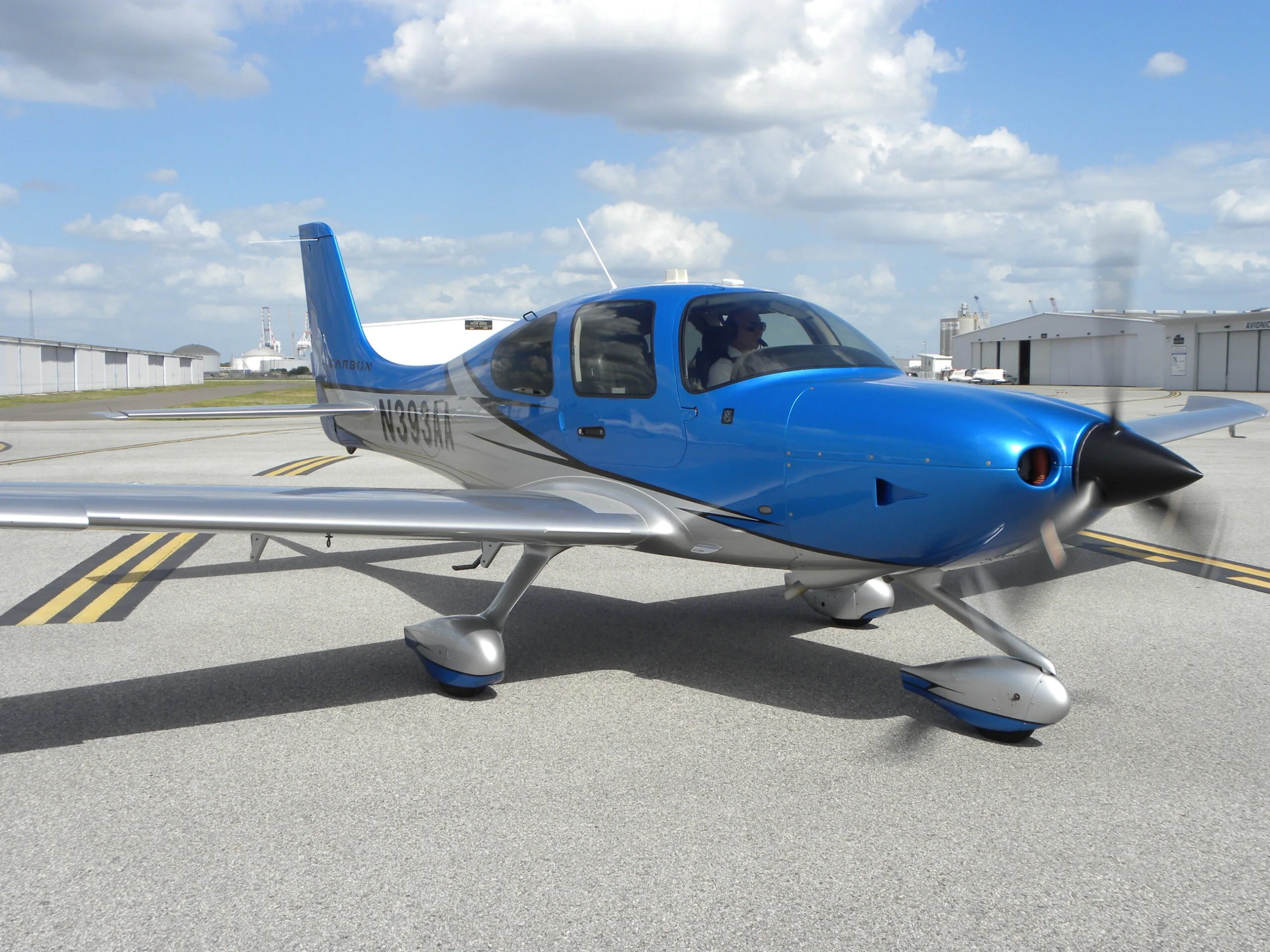 A blue and silver Cirrus SR22 aircraft with registration N393AA, parked on an asphalt ramp with its propeller spinning.