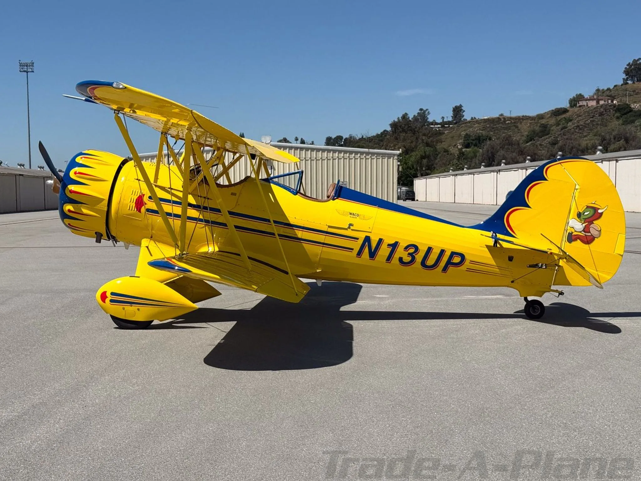A side view of a yellow and blue biplane with registration N13UP parked on an airfield.