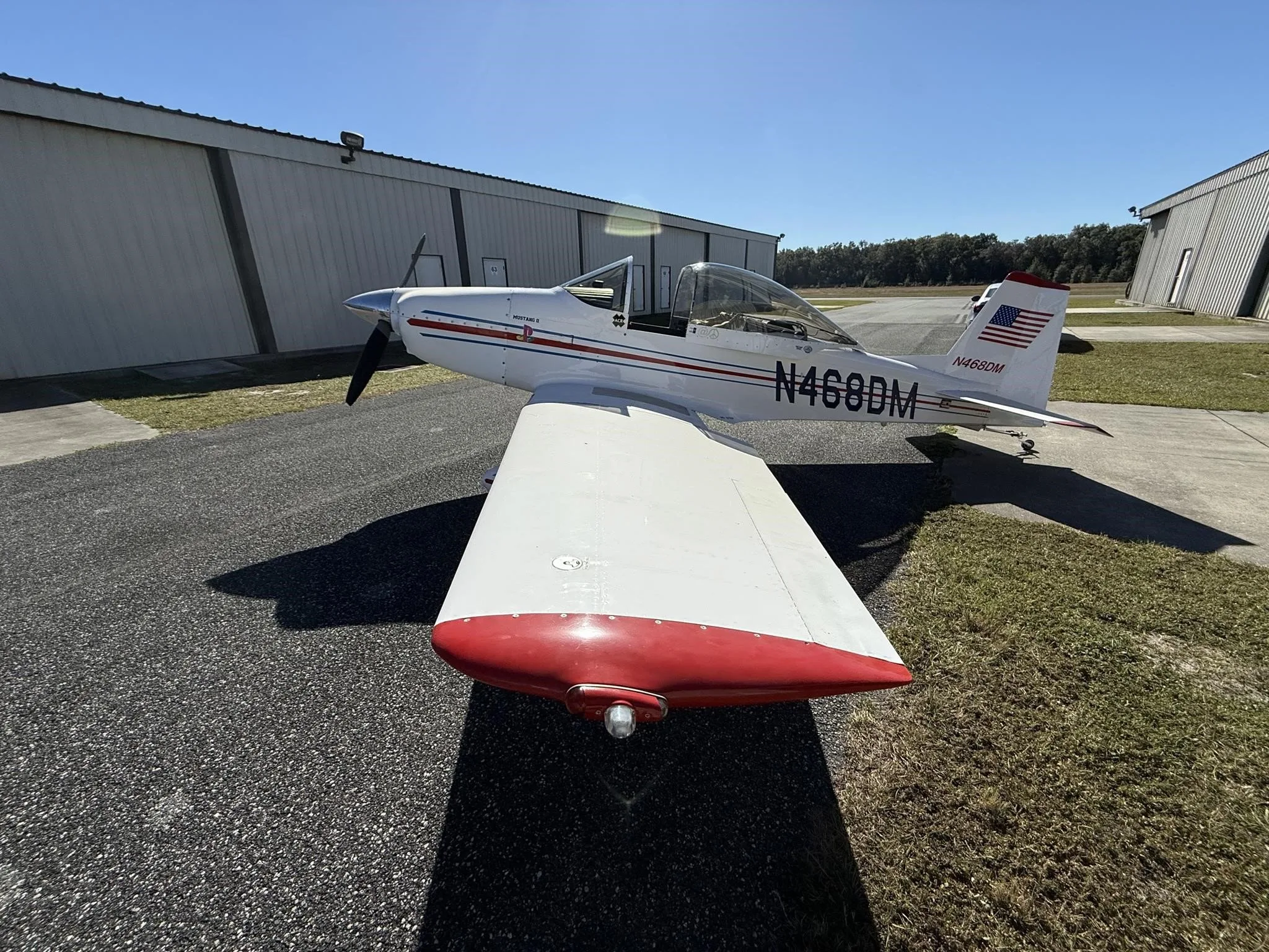A white Mustang II aircraft with red wingtips and blue/red stripes, registration N468DM, parked on a tarmac.