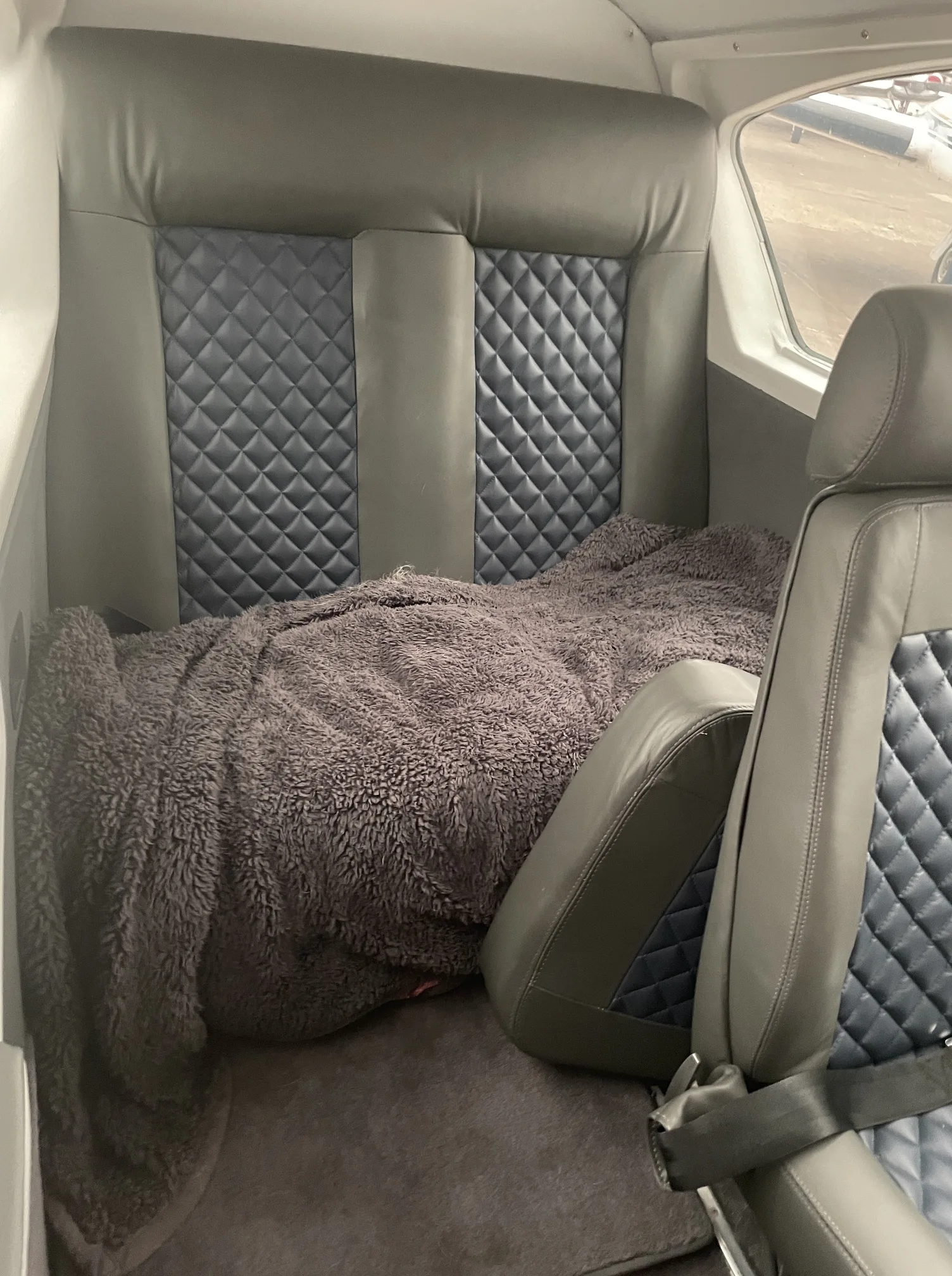 The aircraft's cabin interior with grey and blue quilted leather seats, one covered by a blanket.