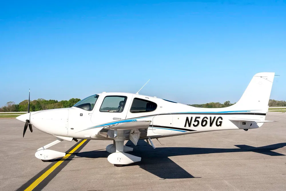 A white Cirrus SR22 aircraft with blue and black stripes, tail number N56VG, parked on an airfield under a clear blue sky.