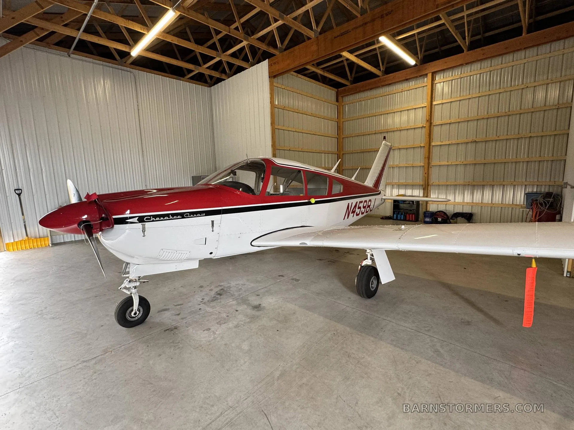 A red and white Piper Cherokee Arrow aircraft, registration N4598J, parked inside a hangar.