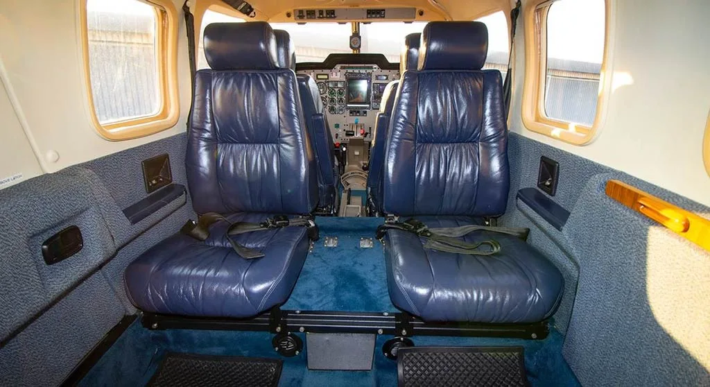 The interior cabin of an aircraft with two rows of blue leather seats and a view towards the cockpit.