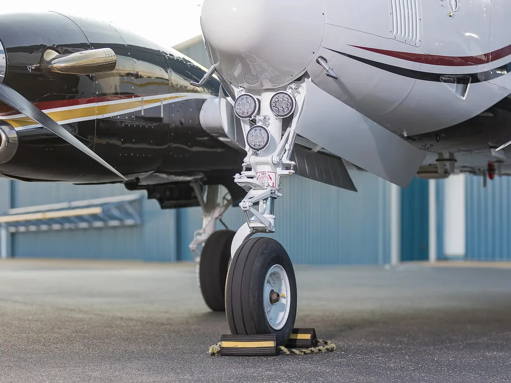 A close-up view of the nose landing gear and lower fuselage of a white and black Beechcraft King Air aircraft.