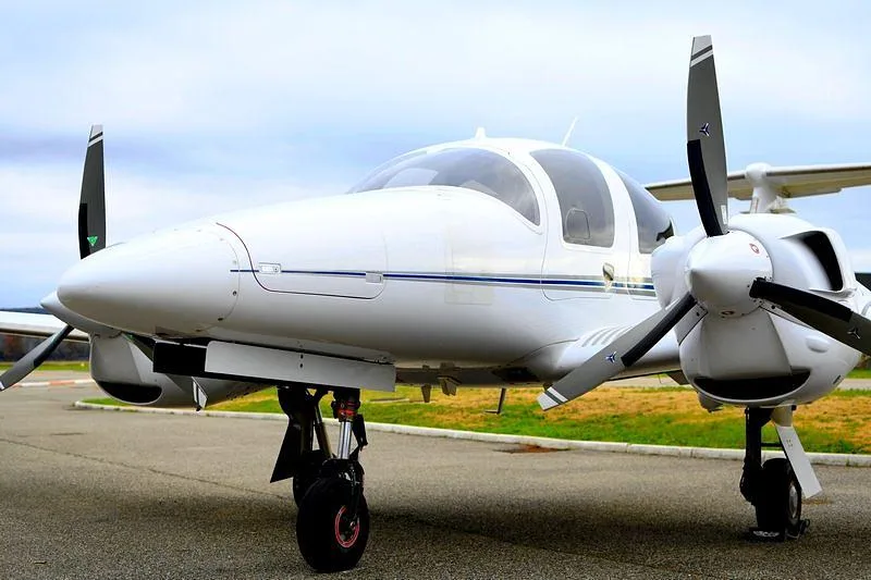 A white Diamond DA62 twin-engine aircraft with blue stripes, parked on an asphalt surface.