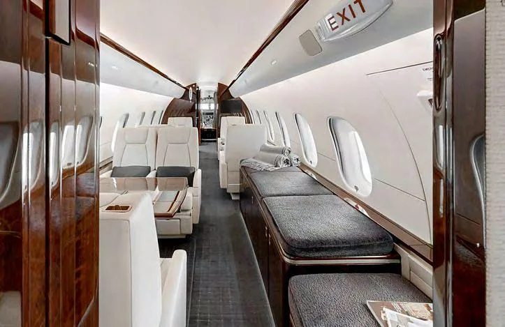 The interior of a private jet cabin with cream seats, a grey divan, and dark wood finishes.