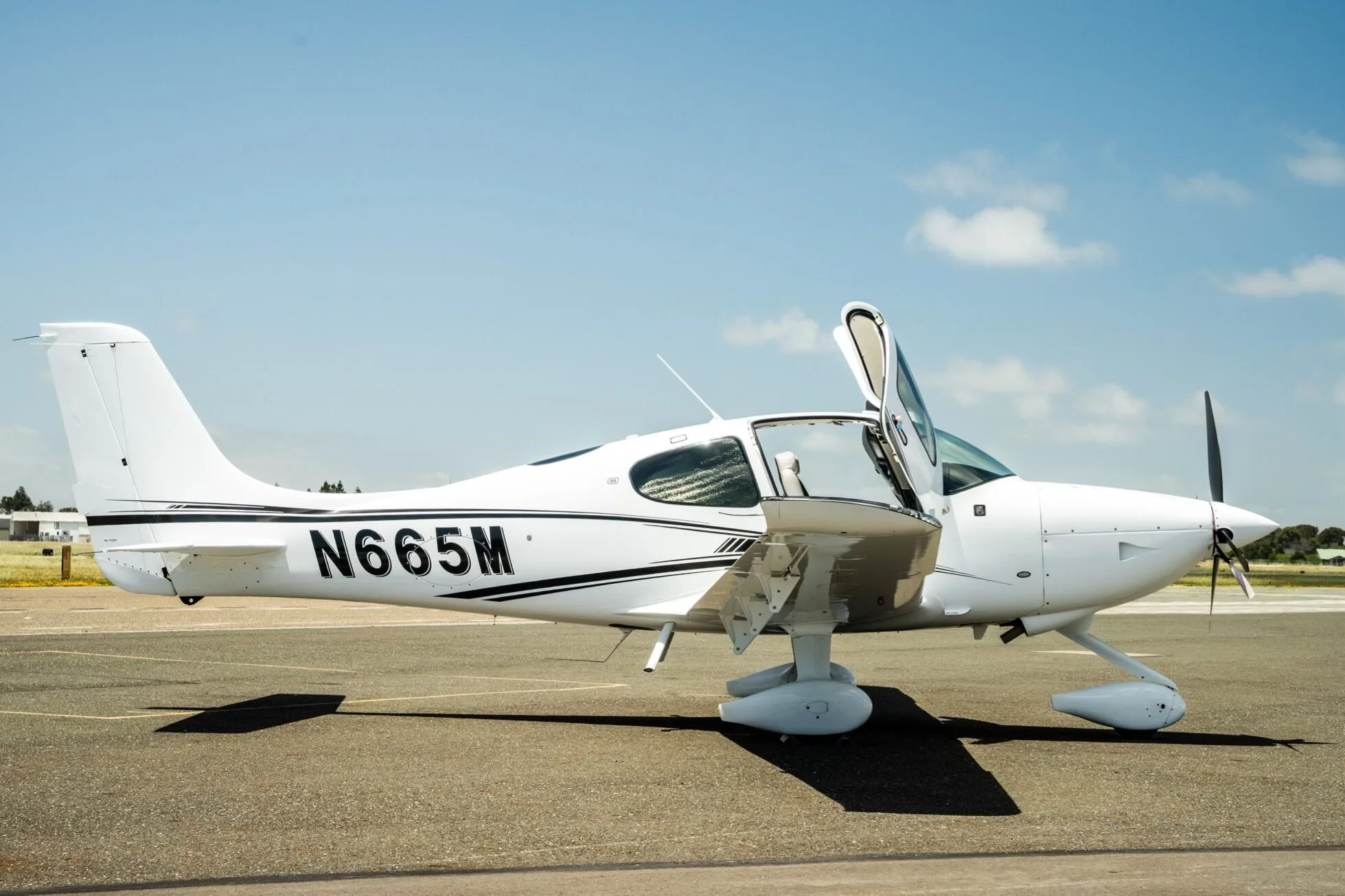 A white Cirrus SR22 aircraft with registration N665M parked on the tarmac with its doors open.