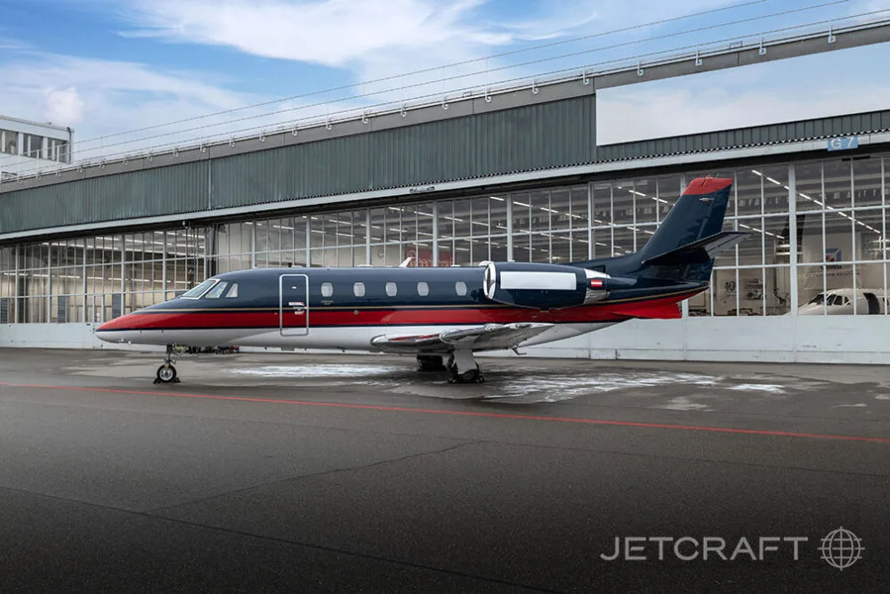 A dark blue, red, and white business jet parked on an asphalt apron in front of a hangar.