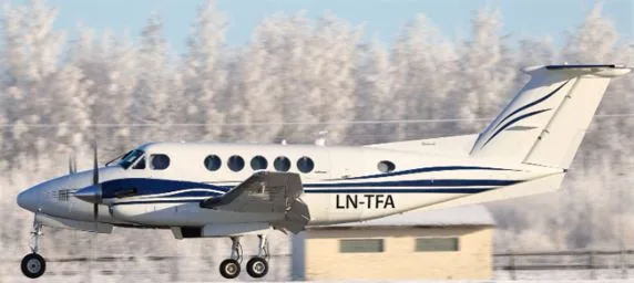 A white and blue turboprop aircraft with registration LN-TFA is seen taking off or landing on a snowy runway with frosted trees in the background.