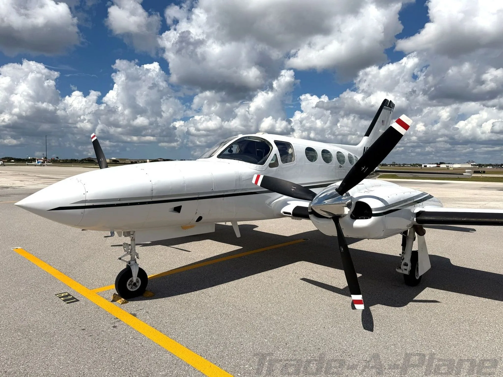 A white Cessna 414 Chancellor aircraft, N720FS, with dark green stripes, parked on an airfield, viewed from the front right showing the propellers.
