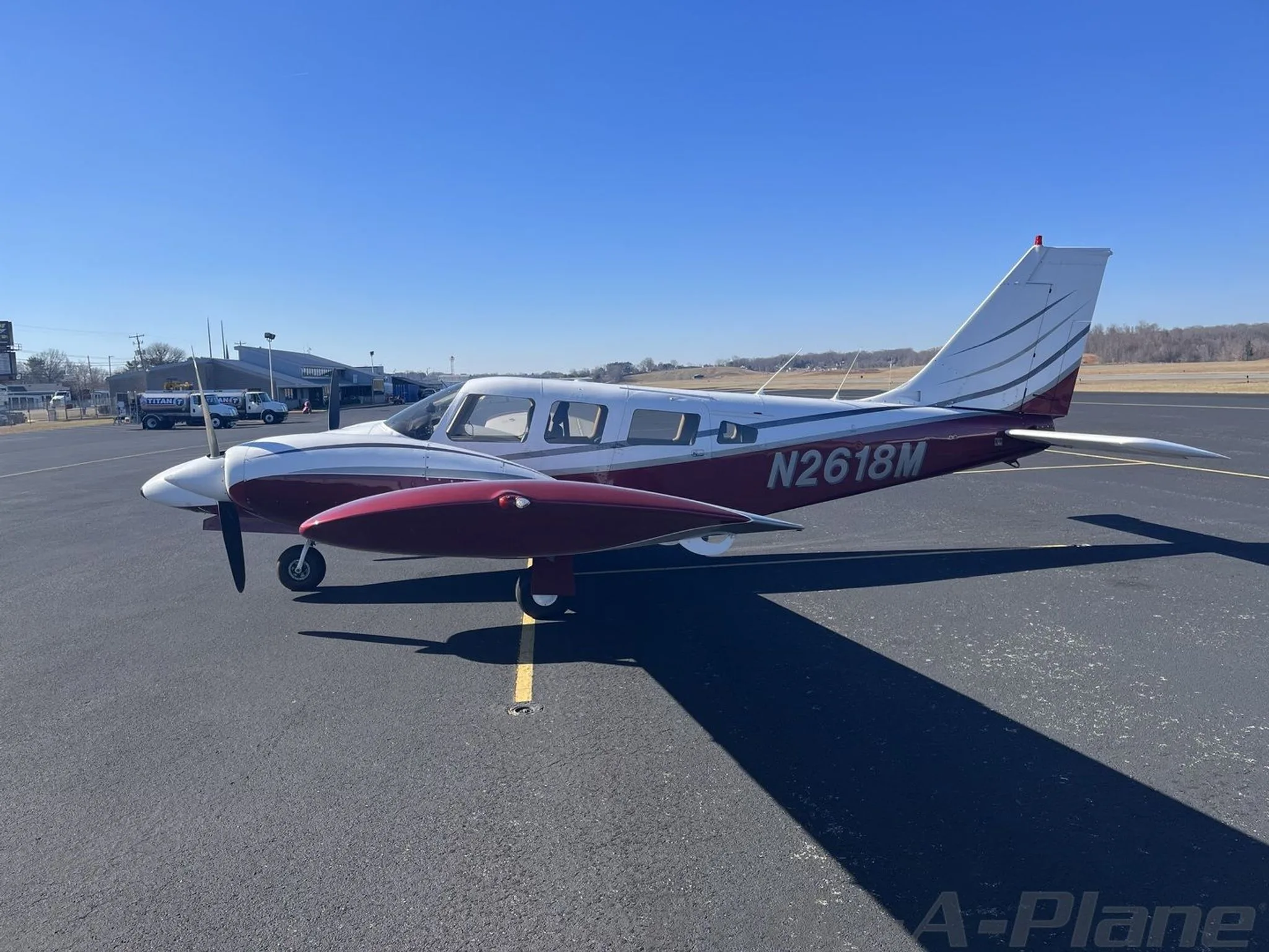 A three-quarter front view of a white and maroon Piper N2618M twin-engine aircraft parked on an airfield.