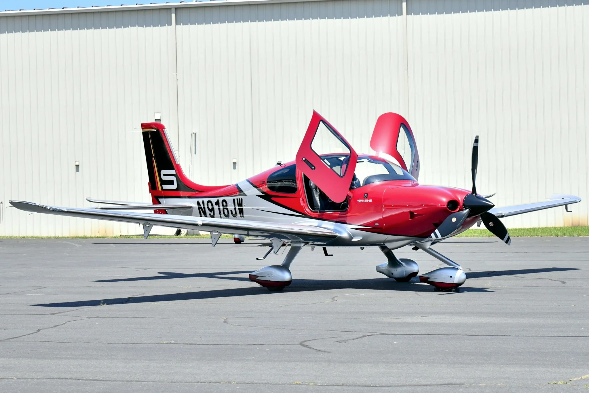 A red and white Cirrus SR22T aircraft with registration N918JW parked on an airfield with its doors open.