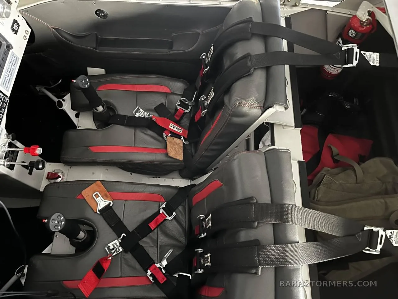 The interior of an aircraft cabin showing two black and red seats with harnesses and a fire extinguisher.
