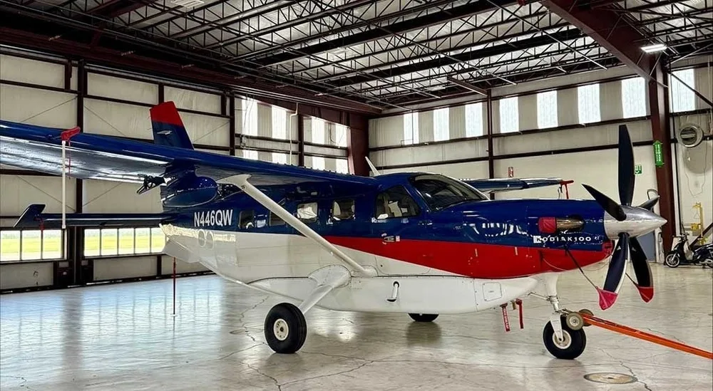 A Kodiak 100 aircraft with a blue, red, and white paint scheme, registered N446QW, parked in a hangar.