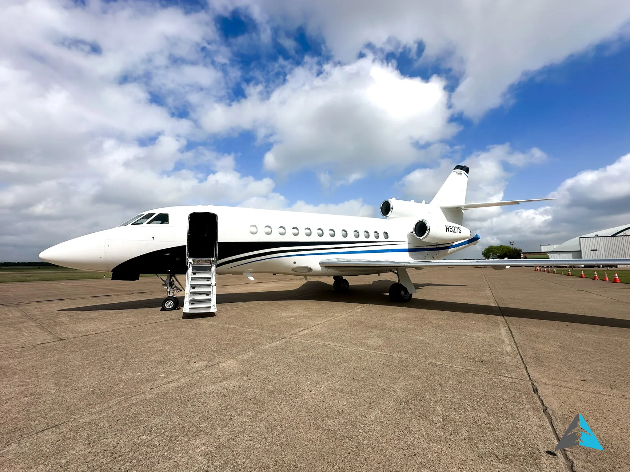 A white Dassault Falcon 900EX business jet with its main door open and stairs extended, parked on an airfield.