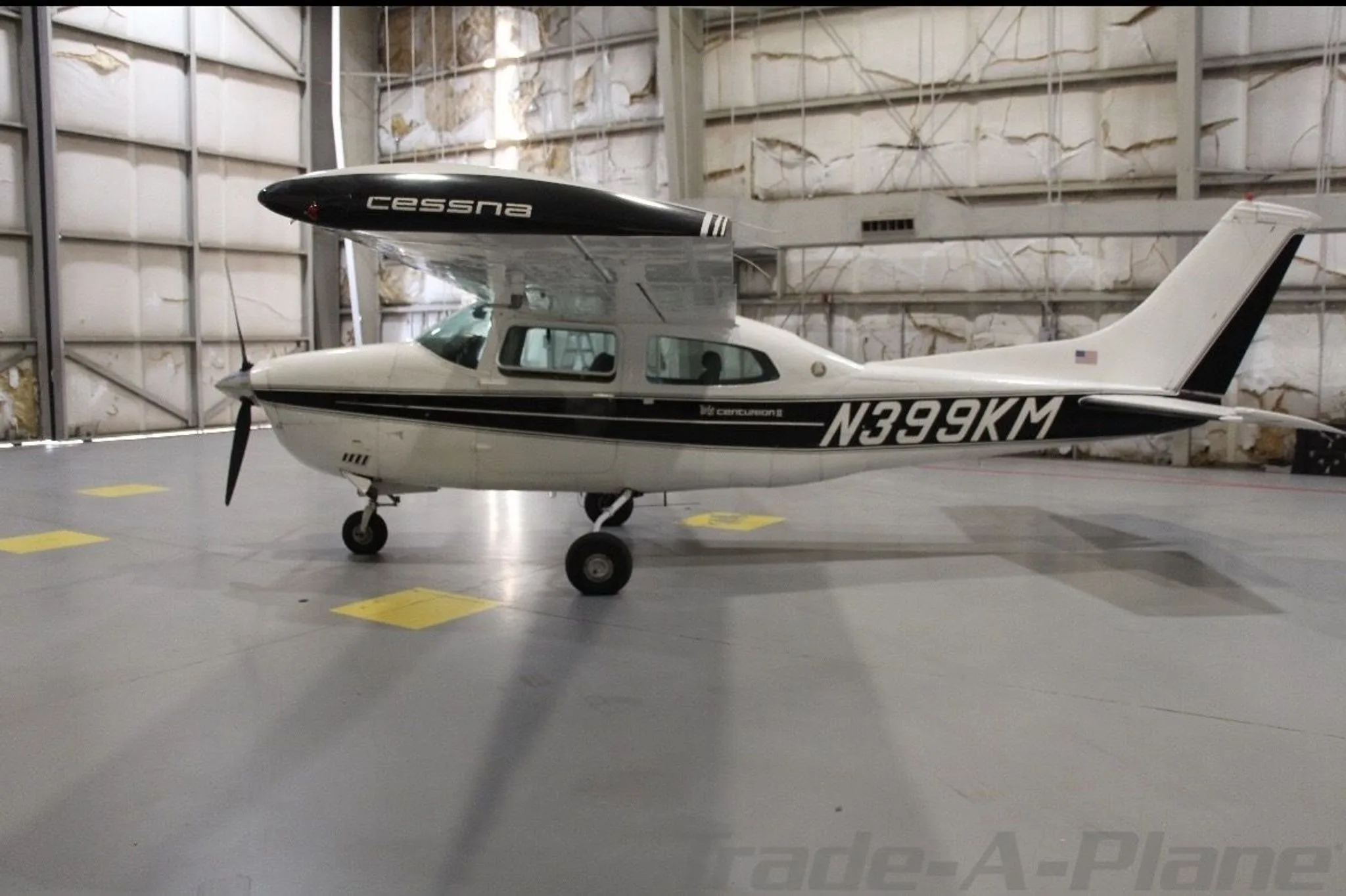 A white Cessna 210 Centurion with black stripes, seen from the left side in a hangar.