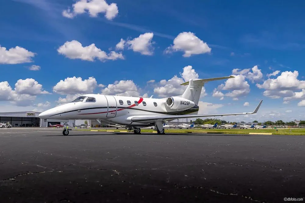 A white business jet with red and black stripes, tail number N428P, parked on an airfield under a blue sky with clouds.