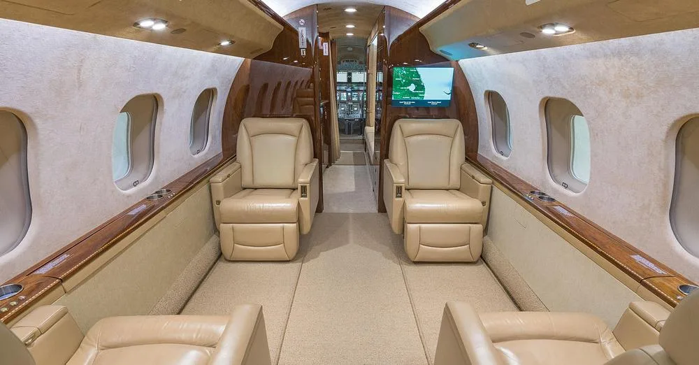 The luxurious cabin interior of a business jet, featuring two beige leather armchairs and a screen displaying a map.