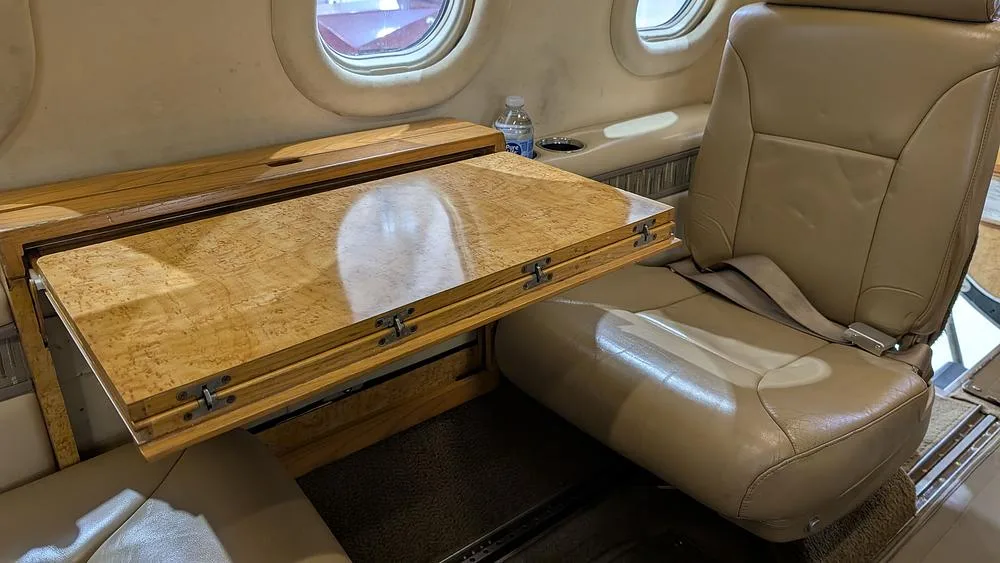 A close-up view of the aircraft's interior showing a beige leather seat and a polished wooden fold-out table.