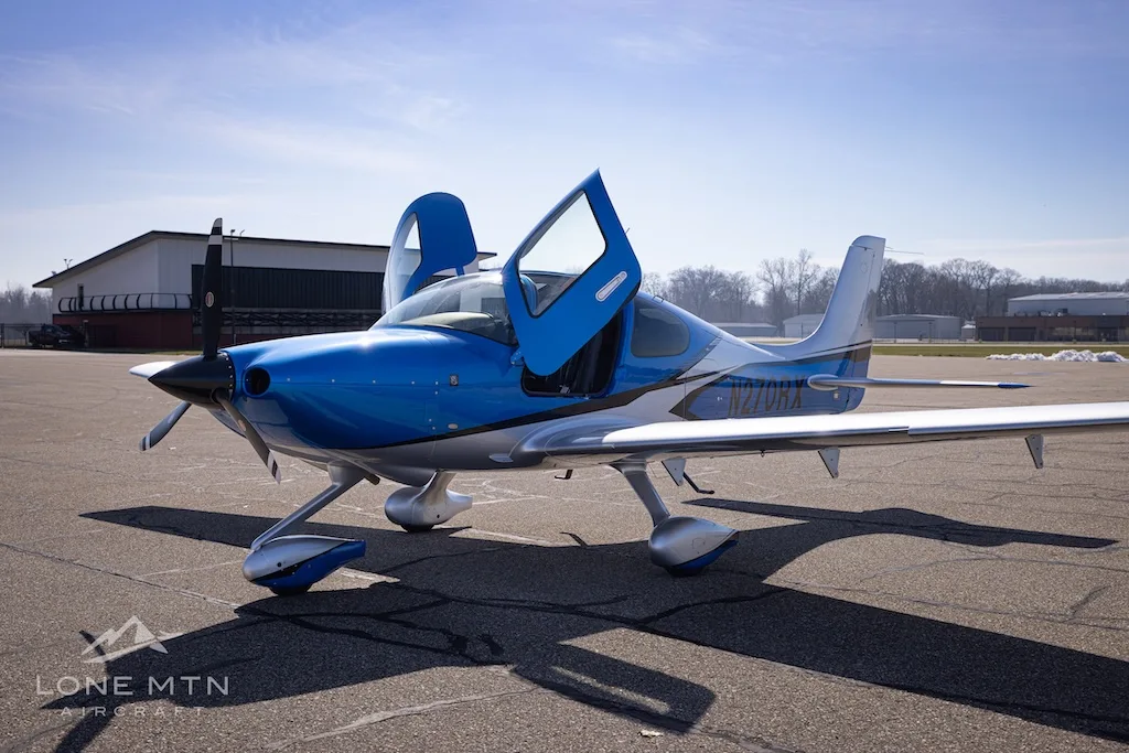 A blue and silver Cirrus SR20 aircraft, registration N270RX, with its doors open on an airport tarmac.