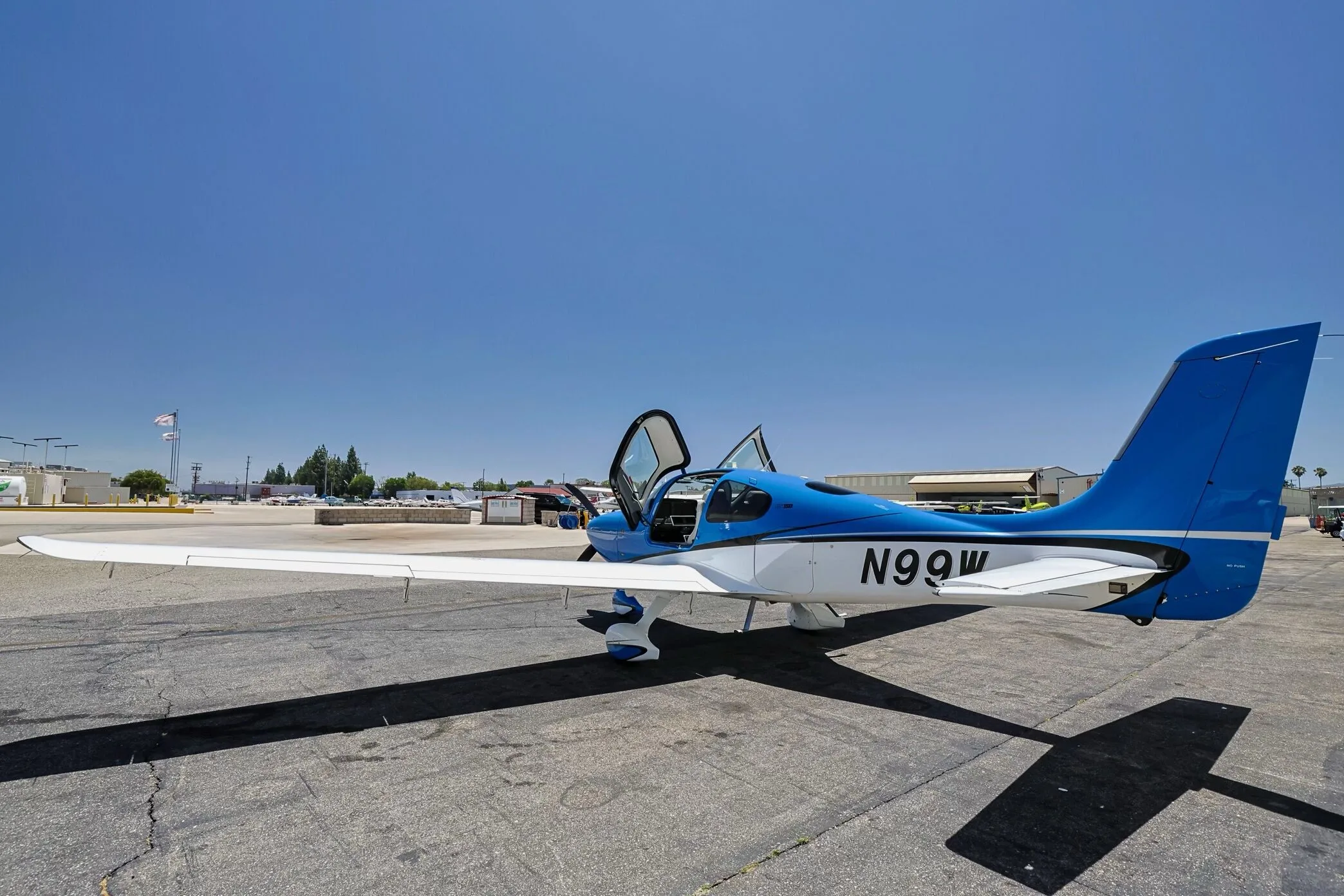 Side view of a blue and white Cirrus SR22 aircraft (N99W) with open doors, parked on an airfield.