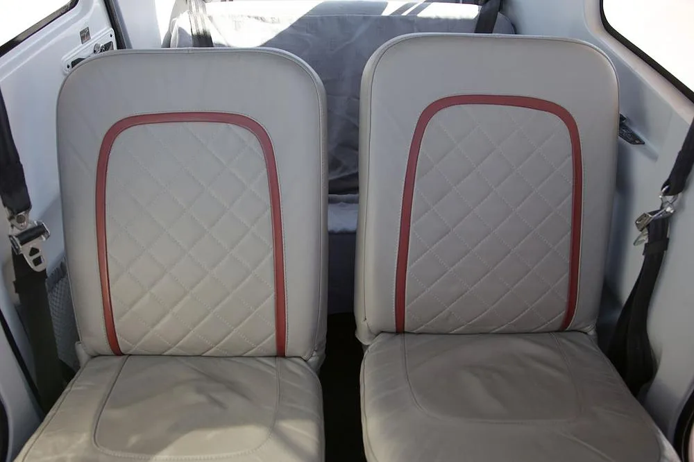 Two light gray aircraft seats with quilted upholstery and red trim.