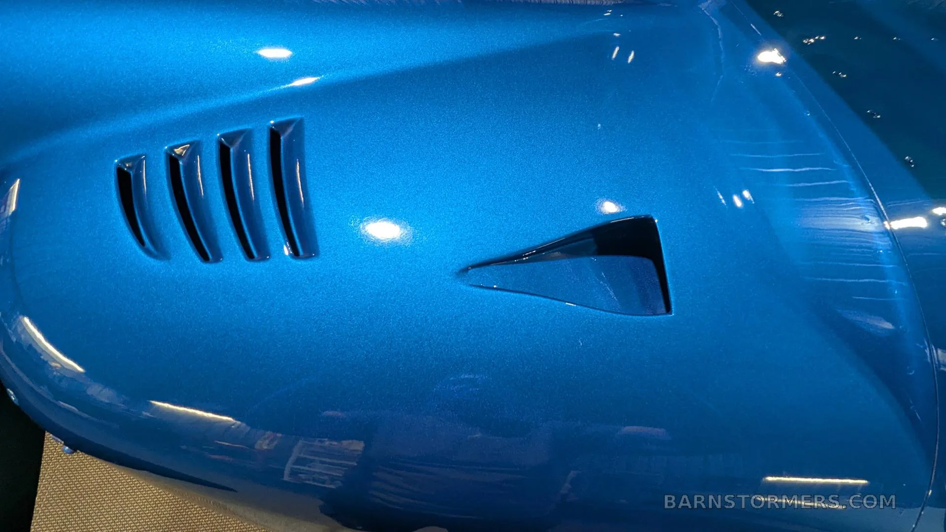 A close-up view of the glossy blue fuselage of an aircraft, showing air vents.