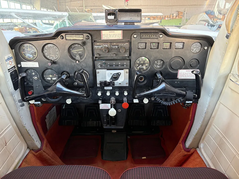 The cockpit instrument panel of a small aircraft showing various gauges, radios, and control yokes.