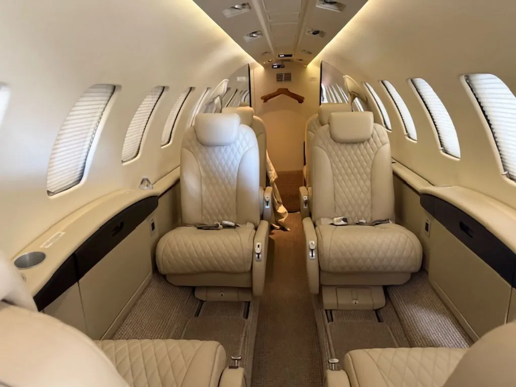 The luxurious interior cabin of a private jet with quilted beige leather seats and window shades.