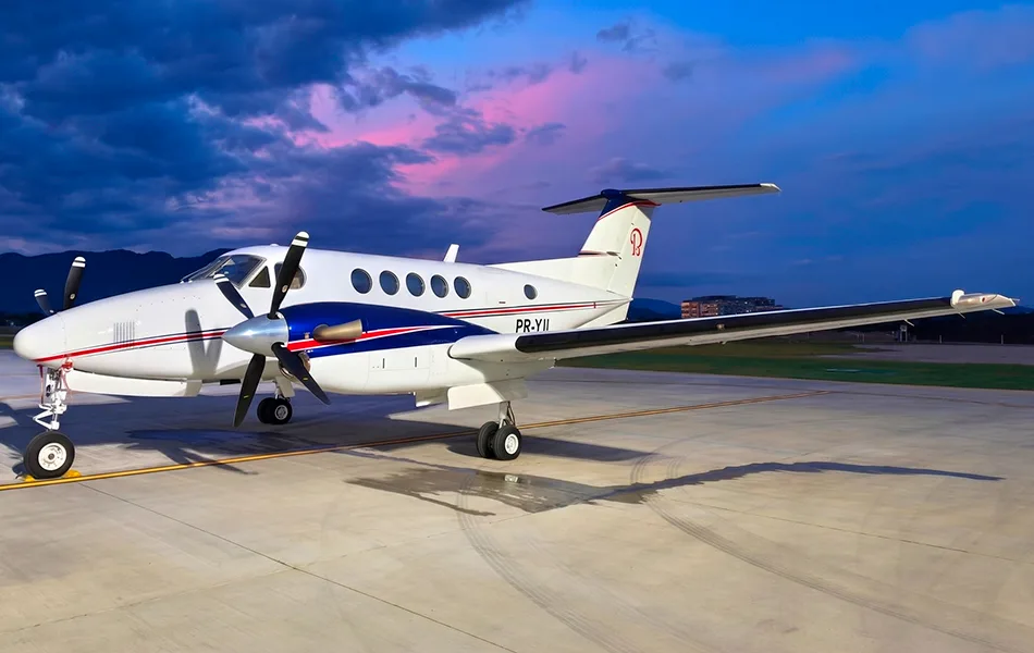 A white Beechcraft King Air turboprop with blue and red stripes is parked on an apron at dusk.