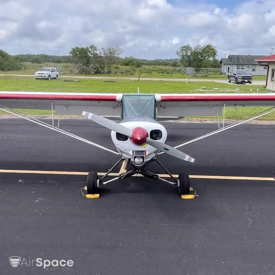A front view of the white high-wing aircraft N3984Z with red stripes, chocked on an asphalt apron.
