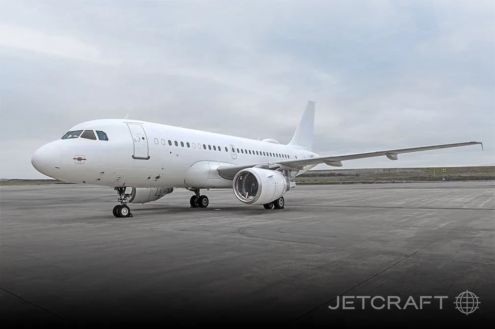 A white Airbus A319 aircraft parked on an airport tarmac under a cloudy sky.