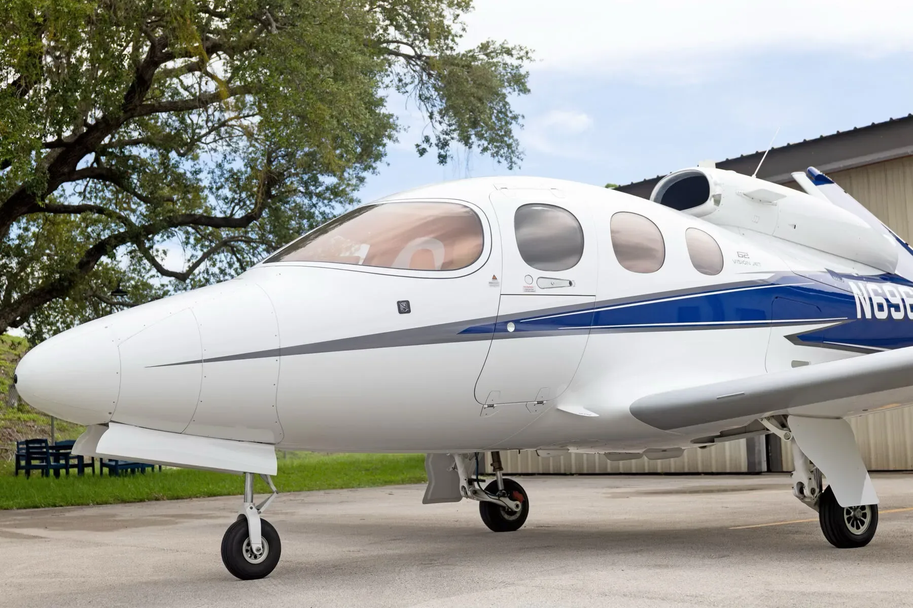 A close-up view of the front fuselage of the white Cirrus Vision Jet (N696MR) with blue and grey stripes, parked outdoors.