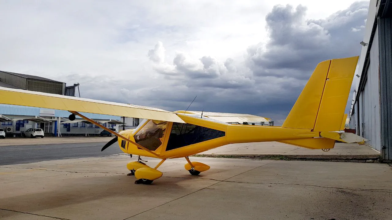 A yellow Aeroprakt-22 aircraft is parked on an airfield tarmac with a cloudy sky in the background.