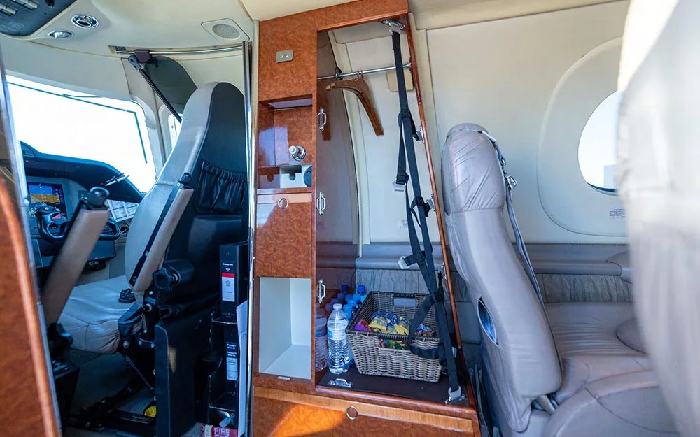 A view inside the aircraft cabin showing a wood-paneled storage unit with a small basket of snacks and a glimpse of the cockpit.