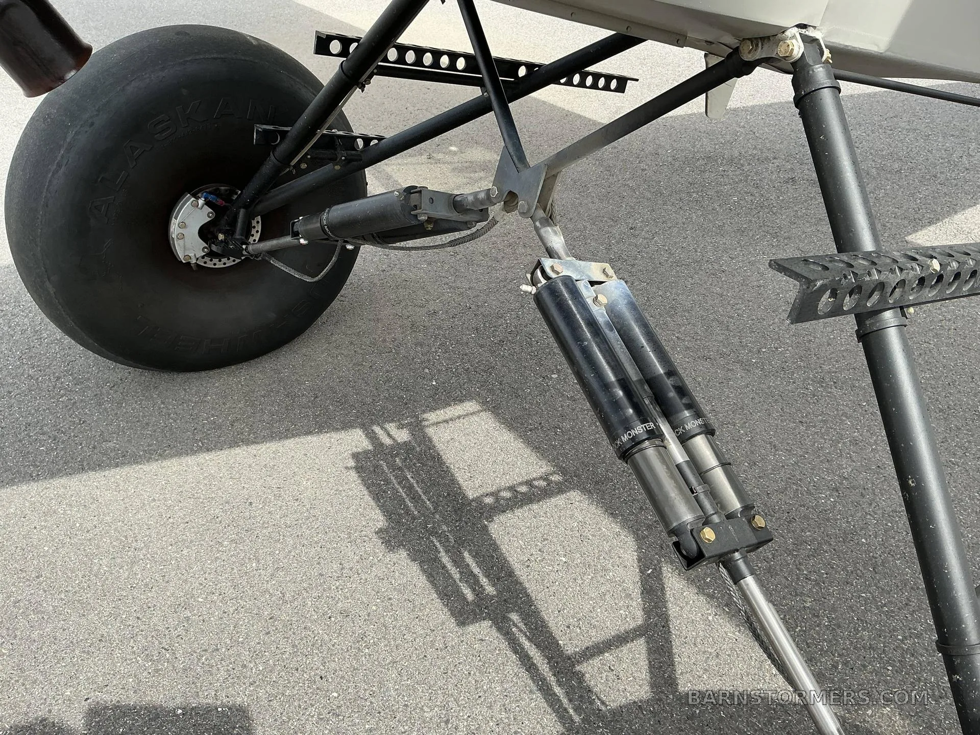 A close-up view of the large "Alaskan Bushwheel" tundra tire and heavy-duty shock absorbers of a taildragger aircraft's main landing gear.