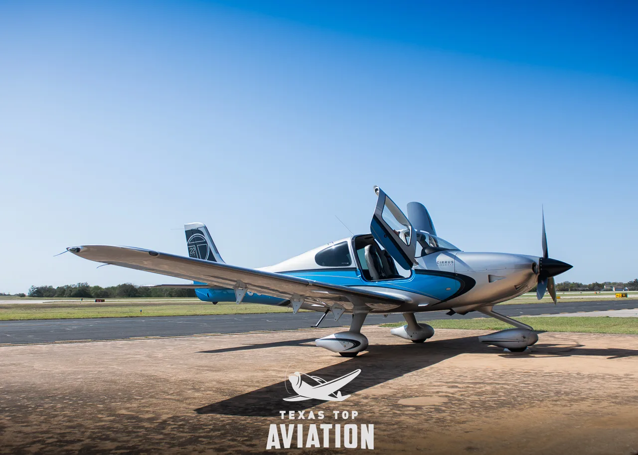 A Cirrus SR22 aircraft with blue and silver paint scheme parked on an airfield with its doors open.