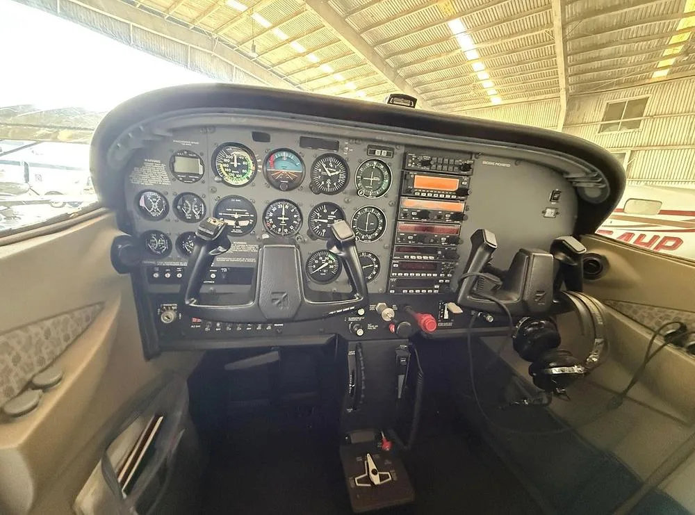 The cockpit of a small aircraft features a full instrument panel with dual yokes and avionics.