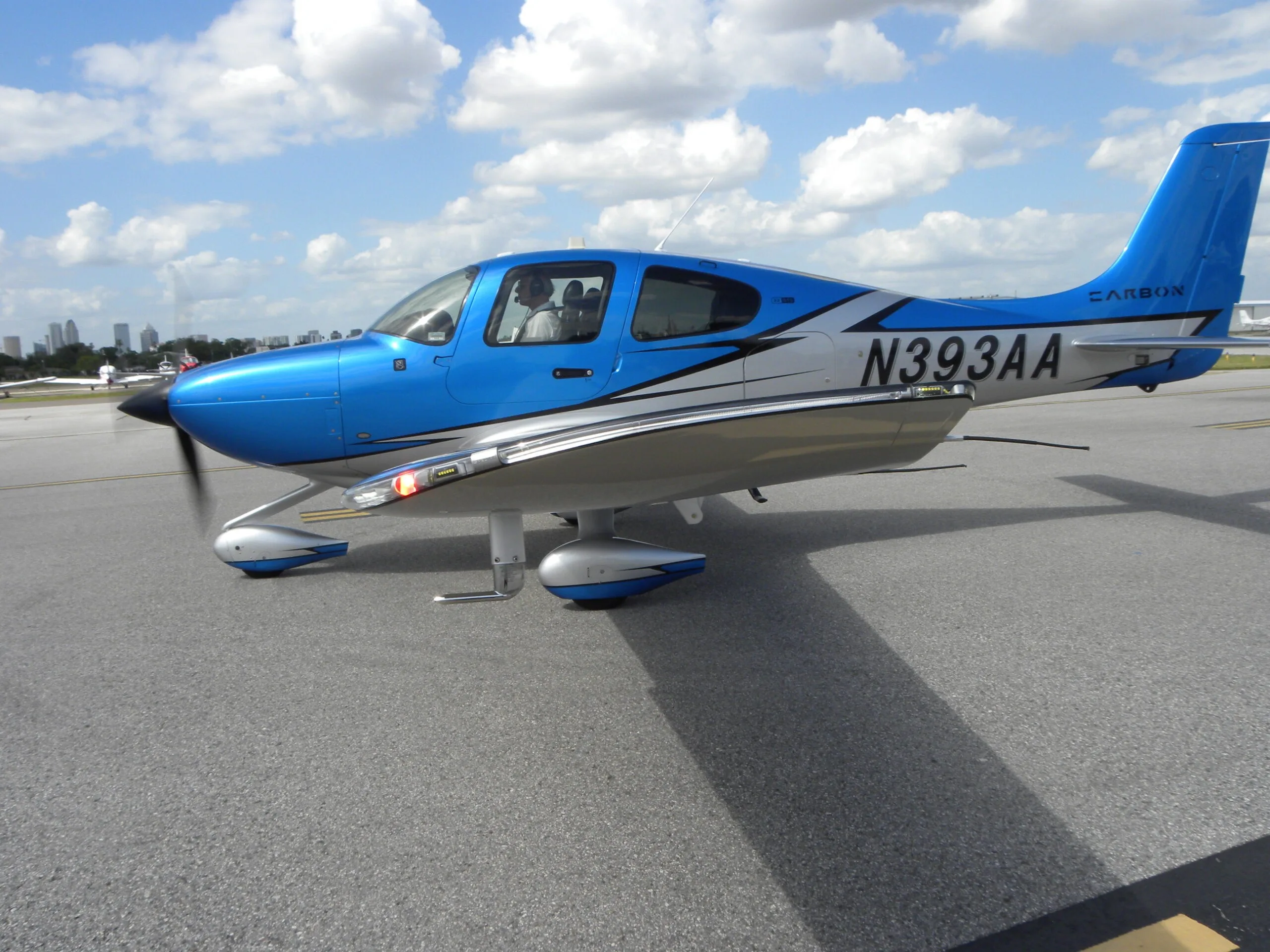 A side view of a blue and silver Cirrus SR22 aircraft with registration N393AA, parked on an asphalt ramp.