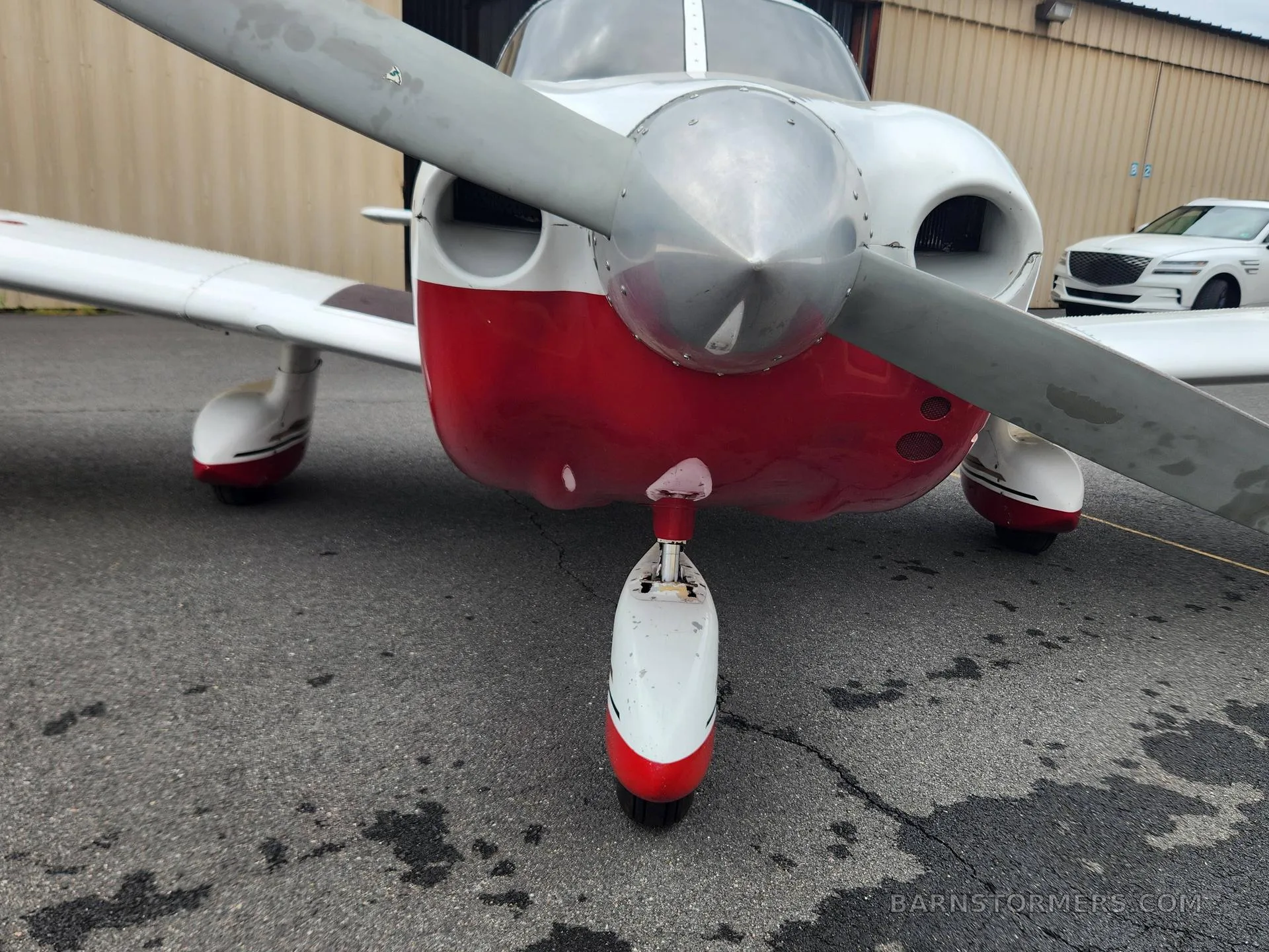 A close-up view of the front propeller and nose gear of a red and white aircraft on asphalt.
