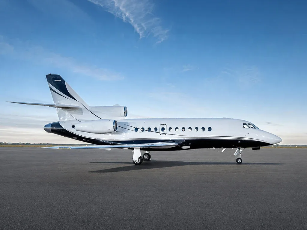 A white business jet with a black and white stripe livery is parked on an asphalt tarmac under a blue sky.