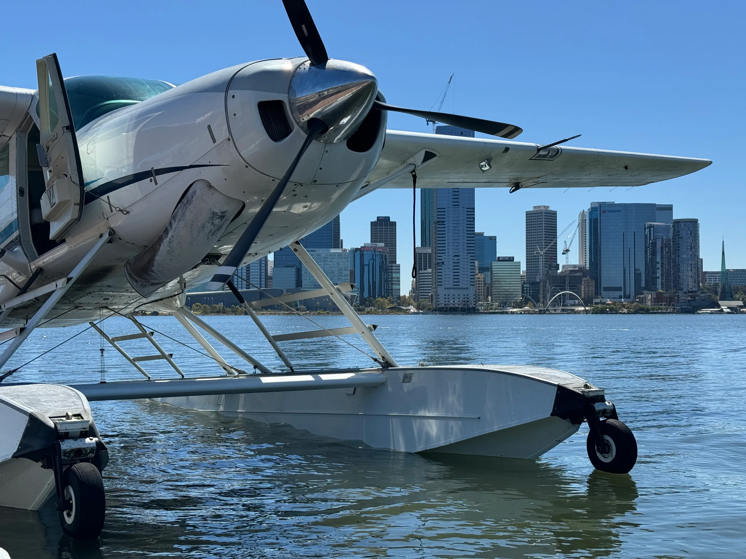 Close-up of a seaplane on the water with a city skyline in the background.